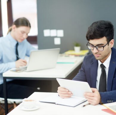 Concentrated young managers in formalwear preparing financial accounts on computers while sitting at modern open plan office